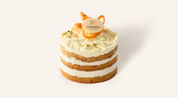 Einzelnes Carrot Cake Törtchen mit drei Schichten Rübenkuchen und cremig-weißer Limetten-Frischkäse-Creme, verziert mit Goldstreuseln und EDUARD'S Logo